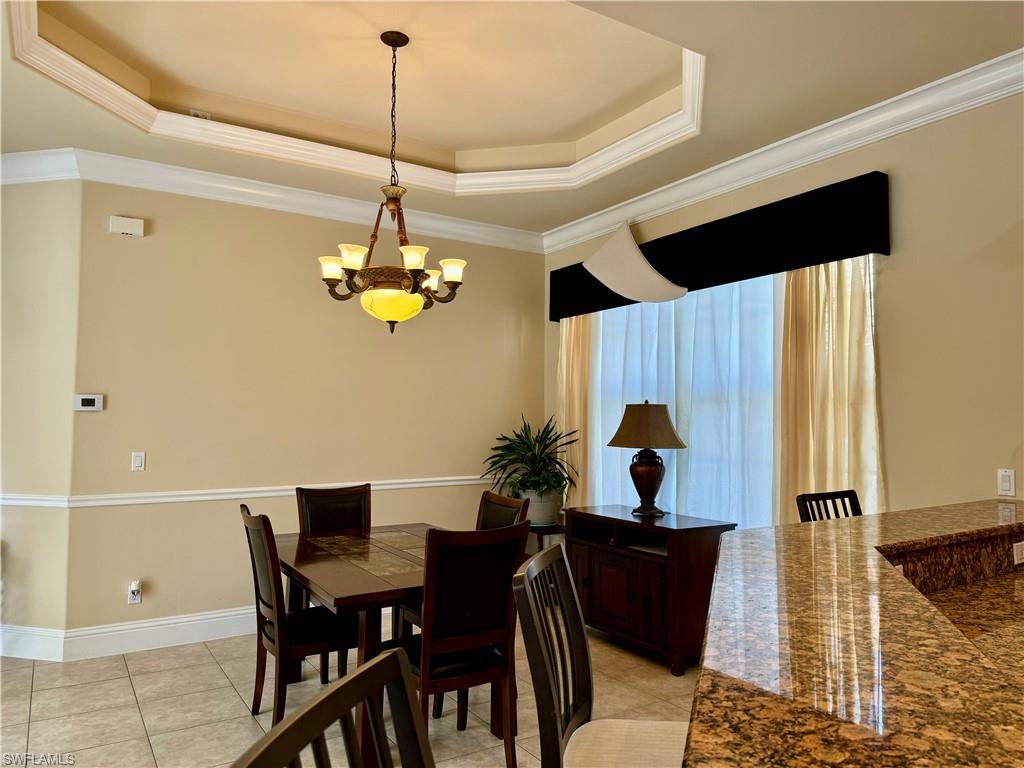 Dining room with a tray ceiling, ornamental molding, a chandelier, and light tile patterned floors
