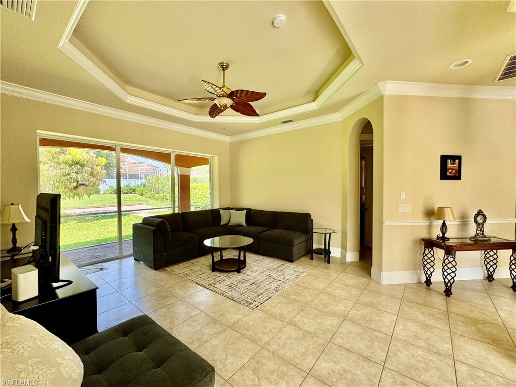 Living area featuring arched walkways, ceiling fan, a tray ceiling, ornamental molding, and light tile patterned flooring
