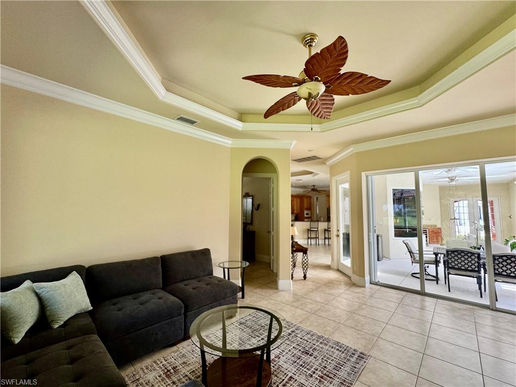 Living room with a tray ceiling, a ceiling fan, ornamental molding, light tile patterned floors, and arched walkways