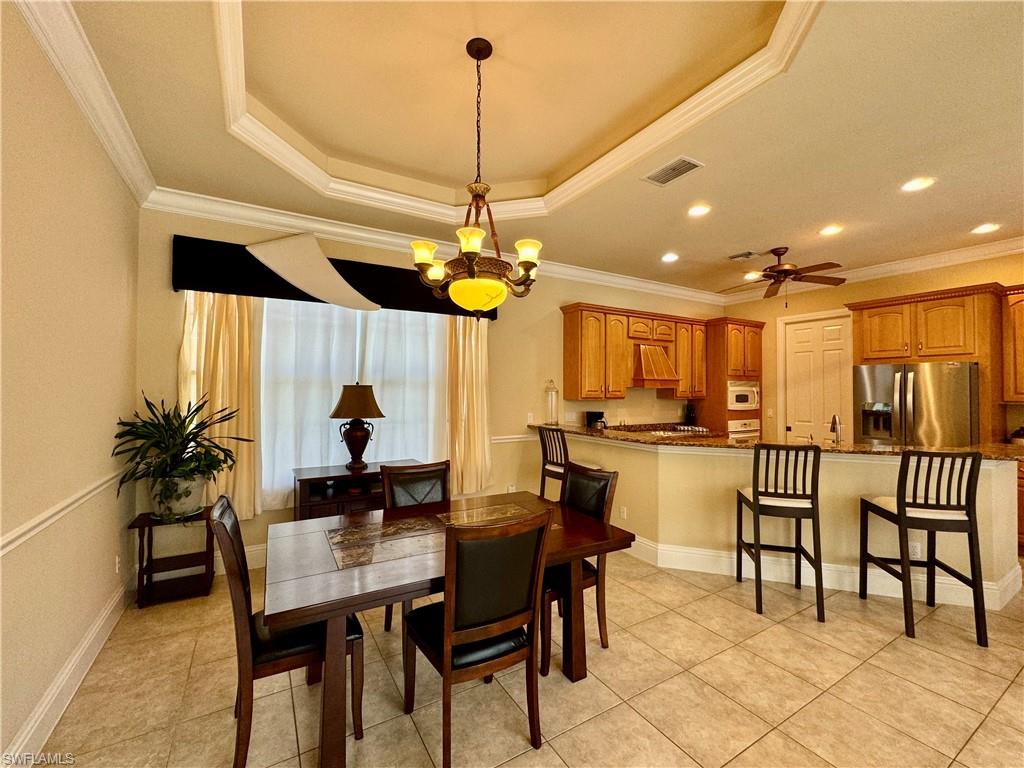 Dining room featuring crown molding, a chandelier, ceiling fan, a raised ceiling, and light tile patterned floors