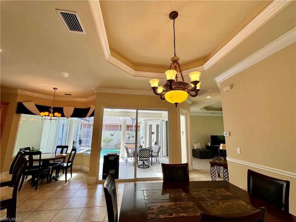 Dining space with a chandelier, a tray ceiling, crown molding, and light tile patterned floors