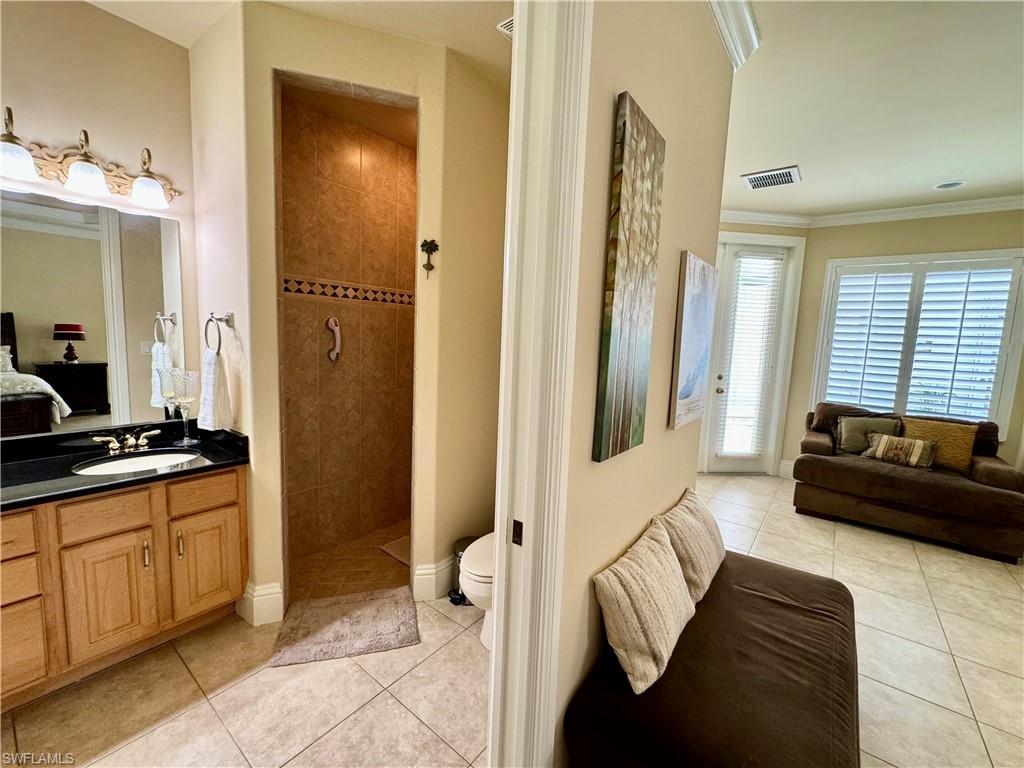 Ensuite bathroom featuring vanity, a walk in shower, light tile patterned flooring, and ornamental molding