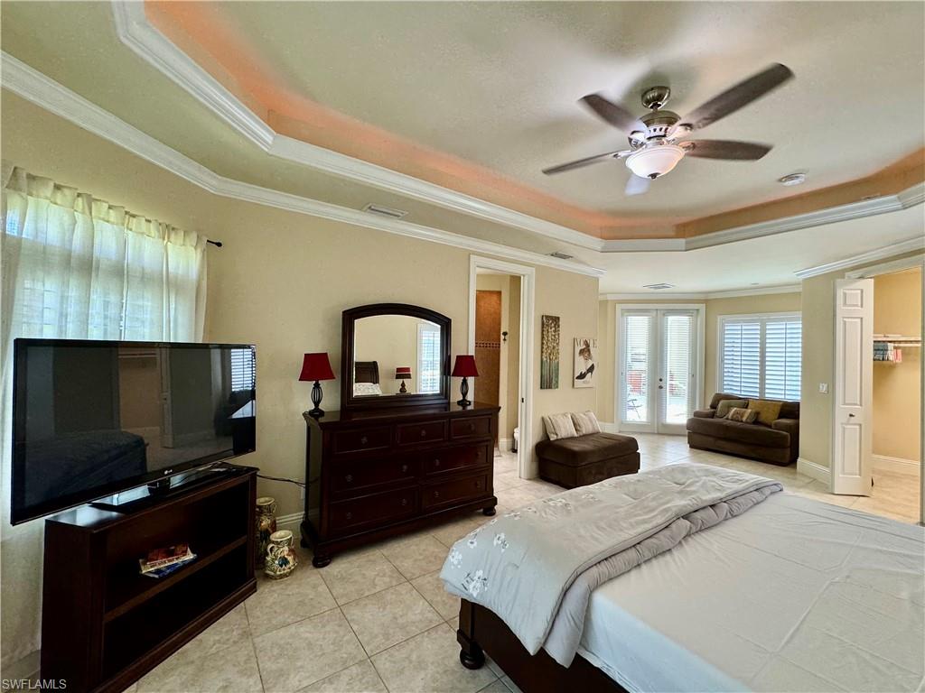 Bedroom with french doors, a tray ceiling, ornamental molding, light tile patterned flooring, and a ceiling fan