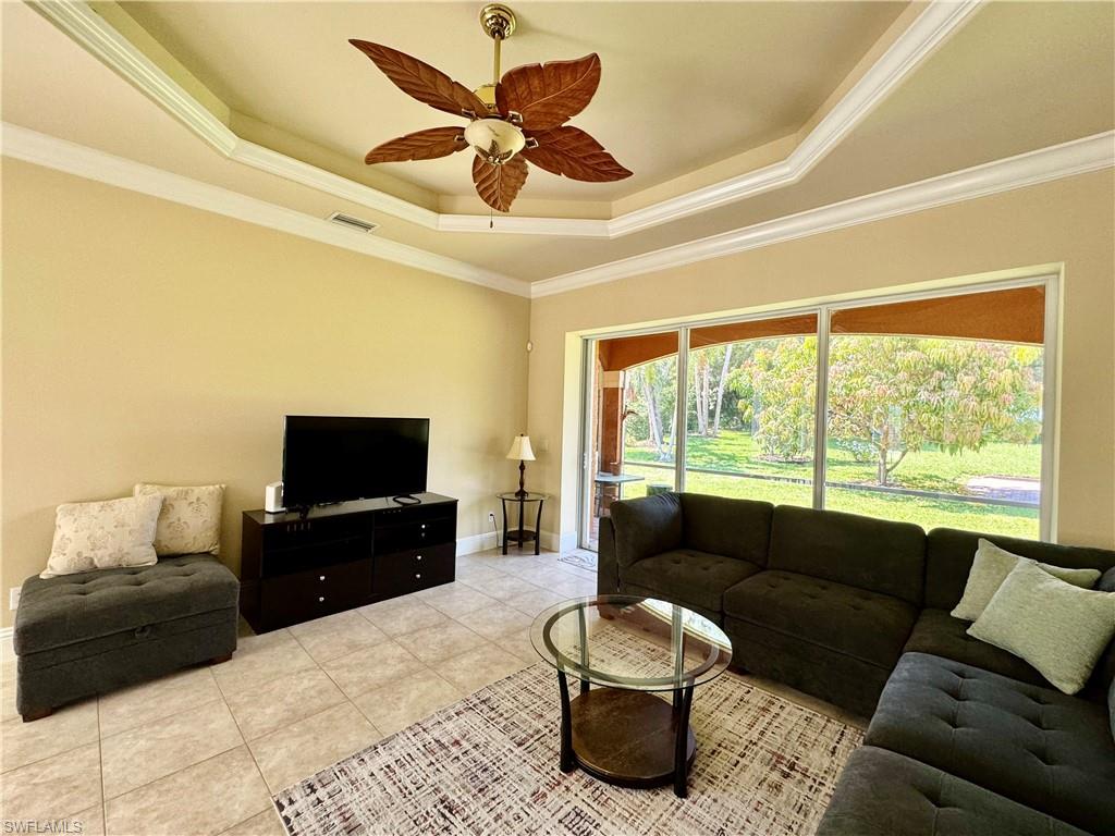 Living area with crown molding, ceiling fan, a raised ceiling, and light tile patterned floors