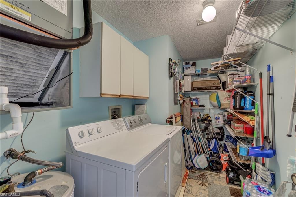 Laundry room featuring a textured ceiling, cabinet space, and washing machine and clothes dryer