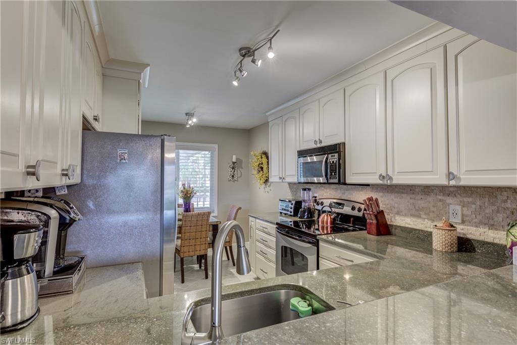 Kitchen featuring stainless steel appliances, white cabinetry, light stone counters, and decorative backsplash