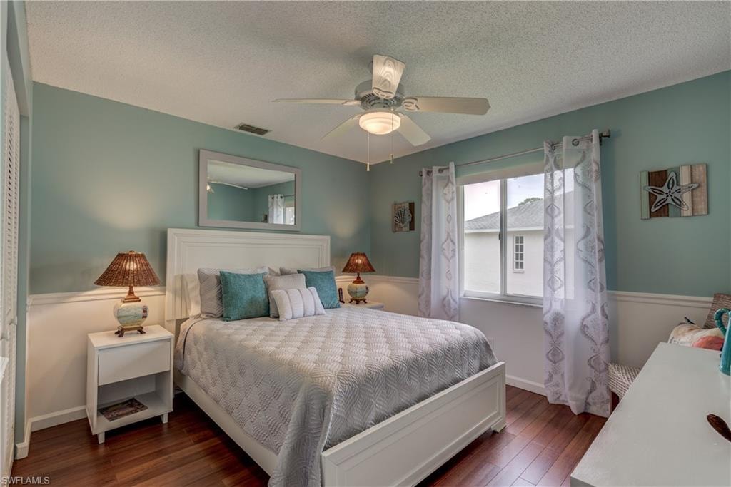 Bedroom with hardwood / wood-style flooring, a ceiling fan, a textured ceiling, and a wainscoted wall