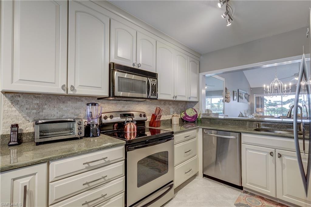 Kitchen featuring stainless steel appliances, dark stone counters, white cabinetry, and vaulted ceiling