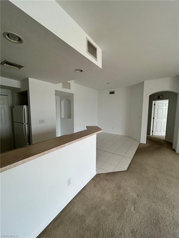 Unfurnished room with arched walkways, light carpet, and light tile patterned floors