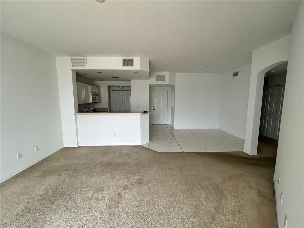 Unfurnished living room with light carpet, arched walkways, and light tile patterned flooring