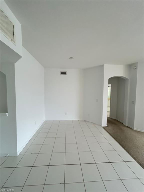 Empty room featuring arched walkways, light tile patterned floors, and light carpet
