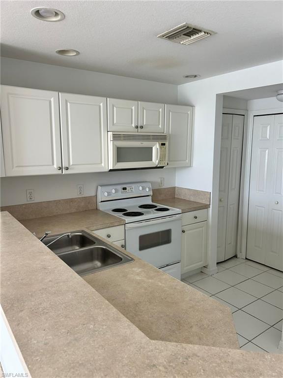 Kitchen with white appliances, light tile patterned flooring, light countertops, a textured ceiling, and white cabinetry
