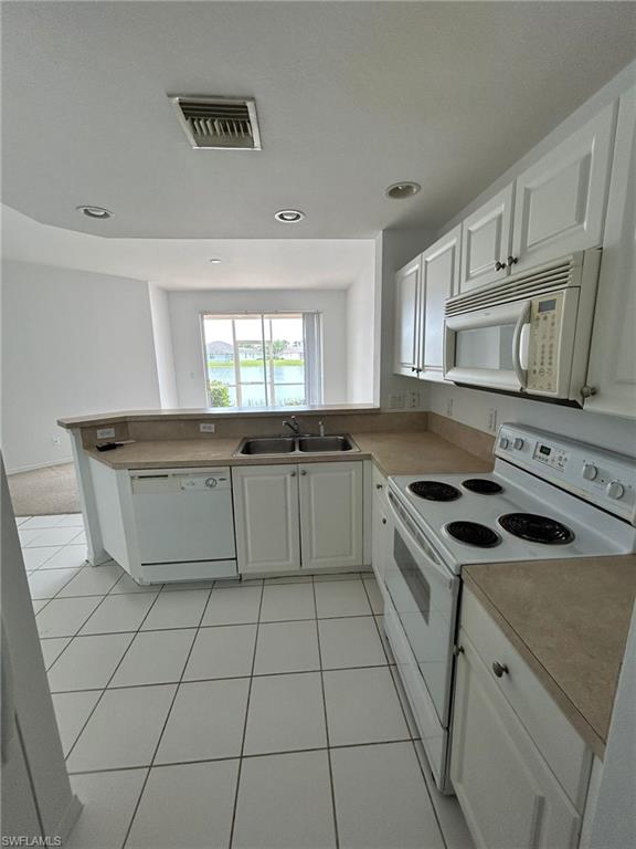 Kitchen with white appliances, white cabinets, a peninsula, light tile patterned floors, and recessed lighting