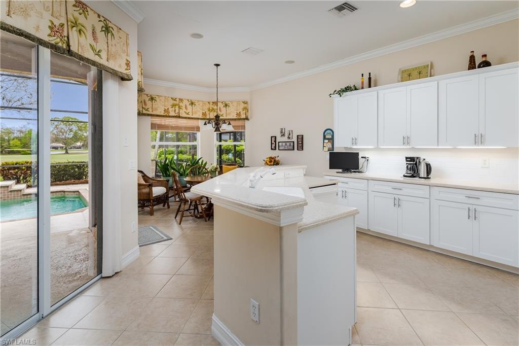 Kitchen with ornamental molding, a center island with sink, white cabinetry, light tile patterned floors, and backsplash