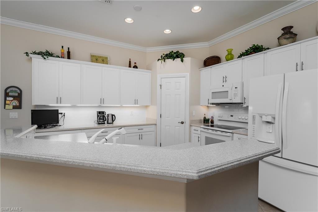 Kitchen with white appliances, white cabinets, ornamental molding, light stone counters, and backsplash