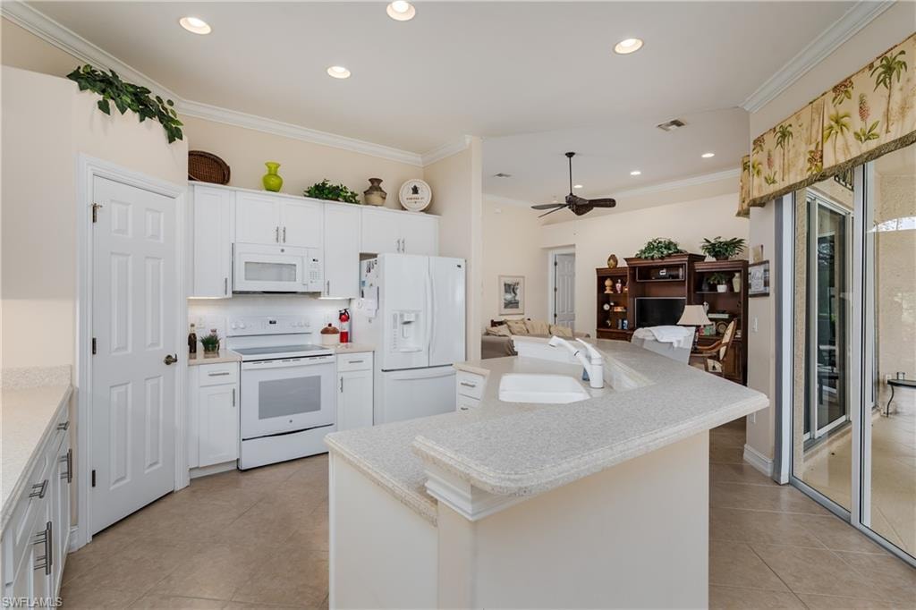 Kitchen featuring white appliances, ornamental molding, a center island with sink, recessed lighting, and tasteful backsplash