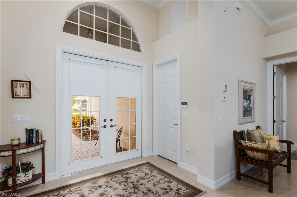 Foyer entrance with french doors, light tile patterned floors, ornamental molding, and a high ceiling