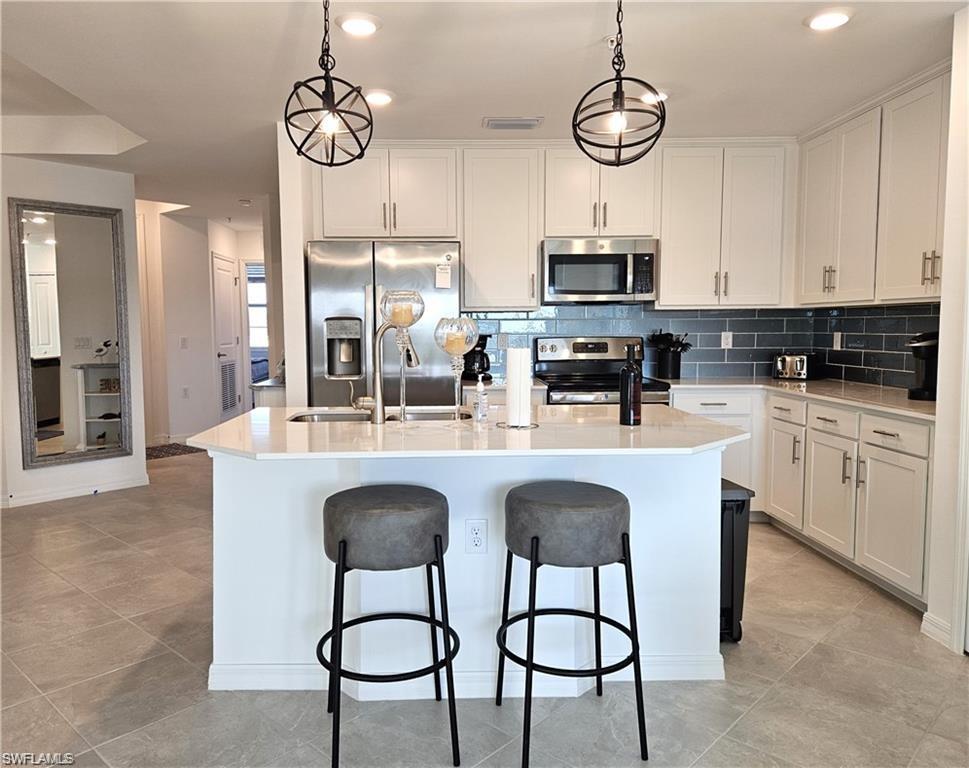 Kitchen with decorative backsplash, stainless steel appliances, a center island with sink, a sink, and a breakfast bar area