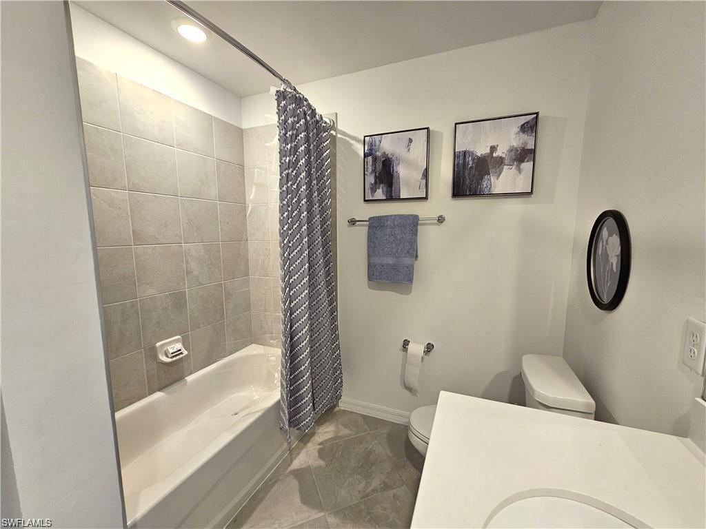 Bathroom with toilet, shower / bath combo with shower curtain, and baseboards