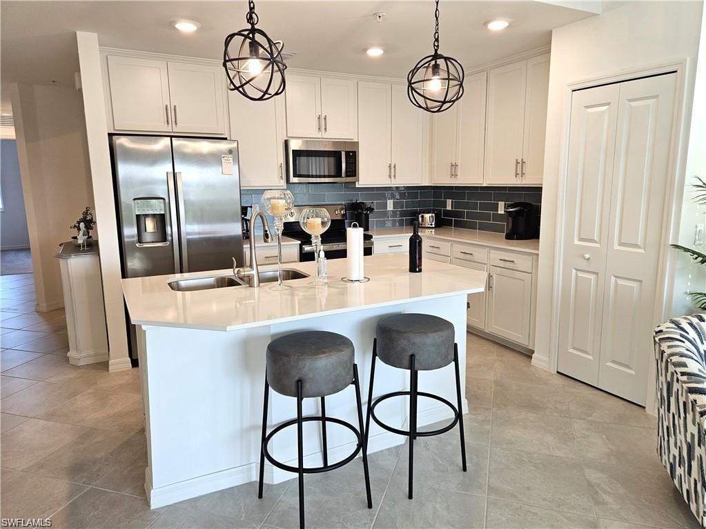 Kitchen featuring stainless steel appliances, tasteful backsplash, white cabinetry, a sink, and an island with sink