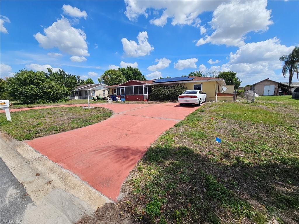Single story home with concrete driveway, solar panels, and a front lawn