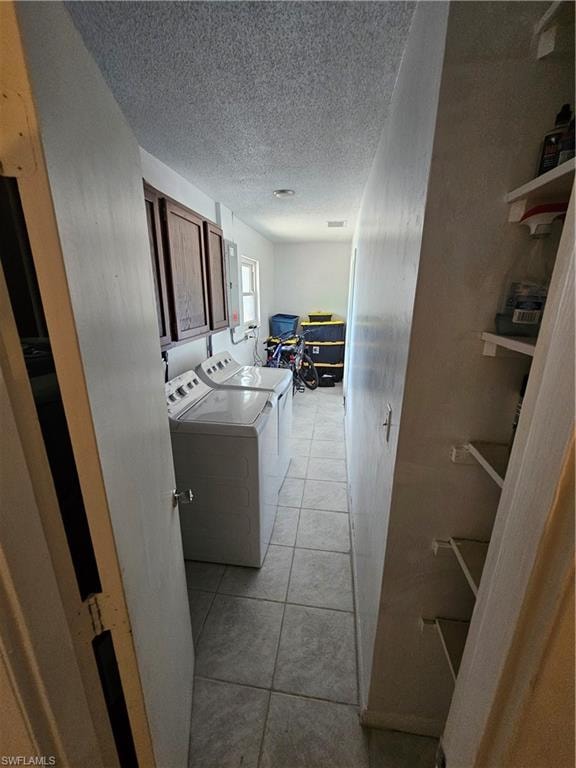Laundry room featuring a textured ceiling, light tile patterned floors, washer and clothes dryer, and cabinet space