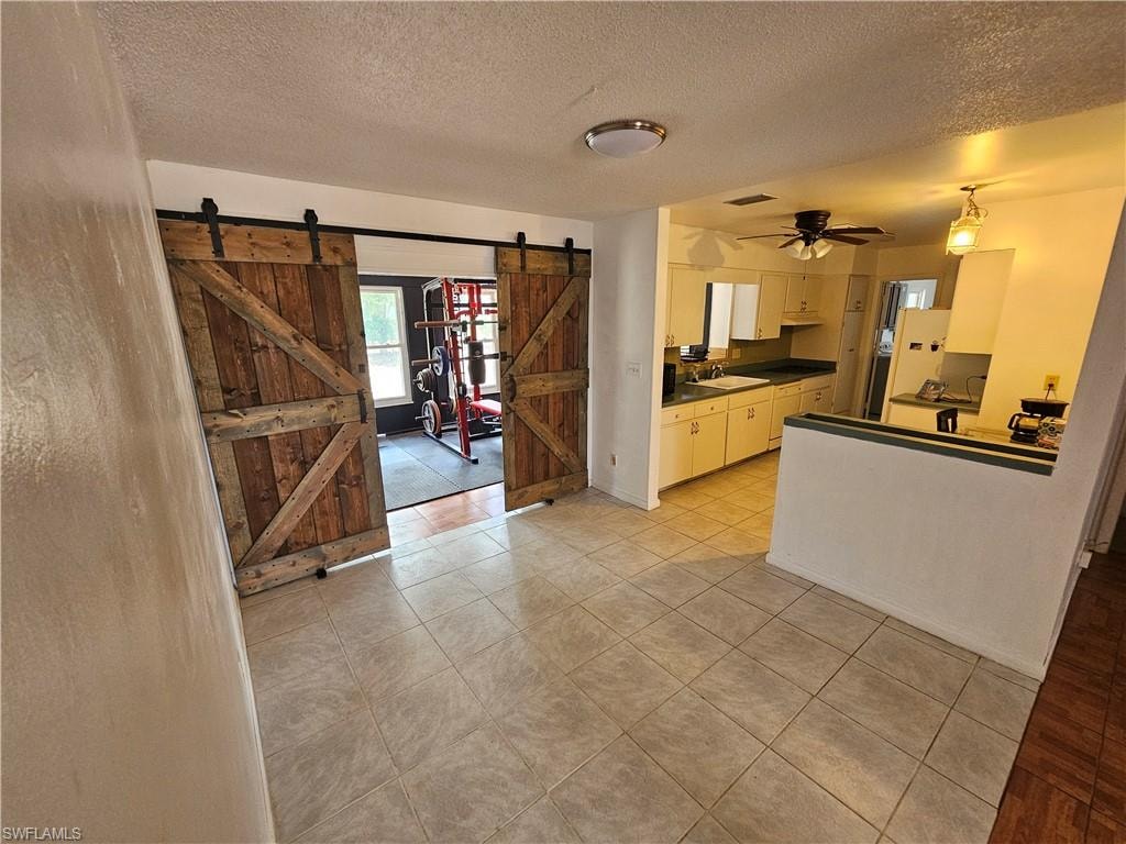 Kitchen with a textured ceiling, ceiling fan, light tile patterned floors, dark countertops, and a barn door