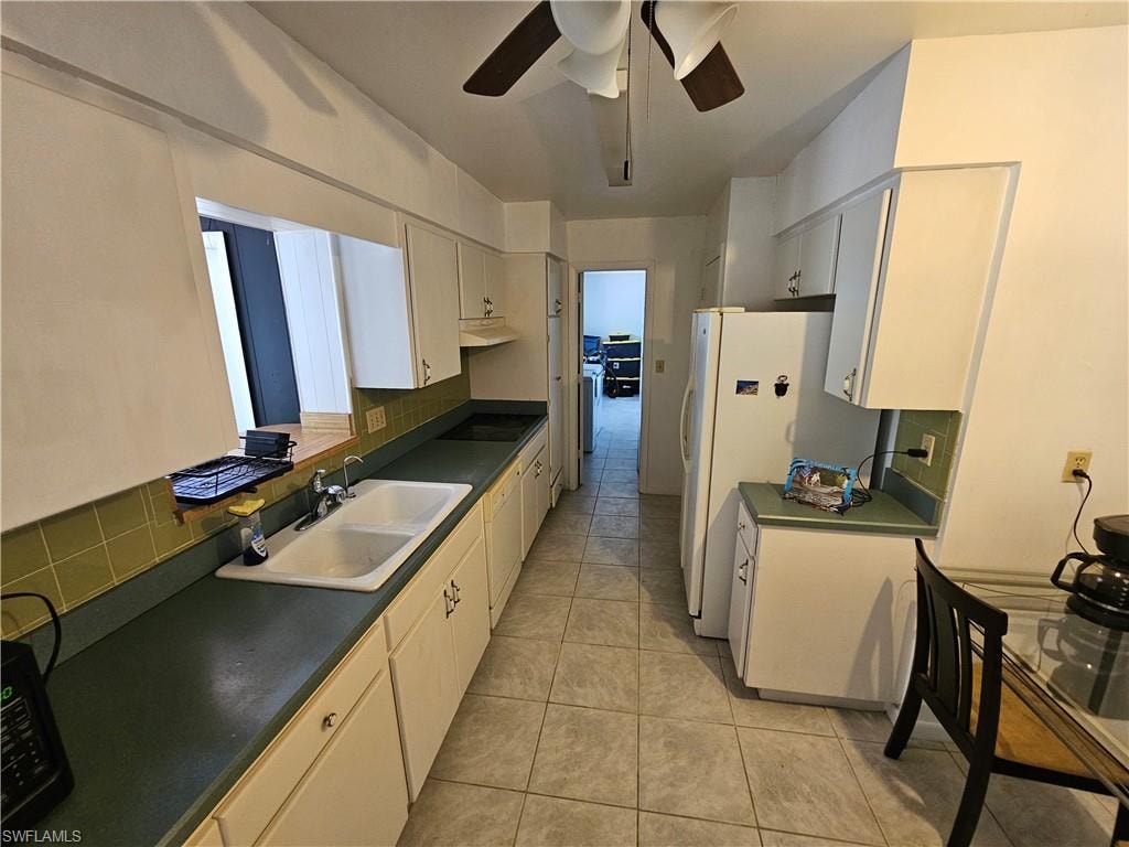 Kitchen featuring decorative backsplash, dark countertops, ceiling fan, freestanding refrigerator, and white cabinets