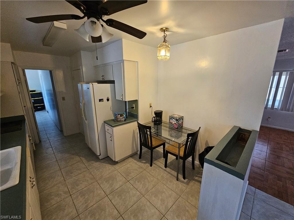 Kitchen featuring white cabinetry, dark countertops, freestanding refrigerator, light tile patterned flooring, and ceiling fan