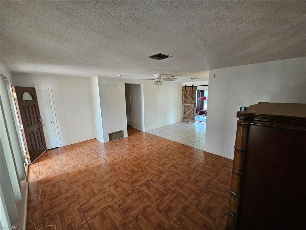 Spare room featuring a barn door, a textured ceiling, and a ceiling fan