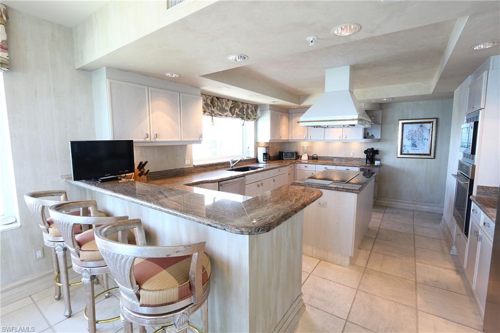 Kitchen featuring a peninsula, island range hood, white cabinetry, a kitchen island, and a kitchen bar
