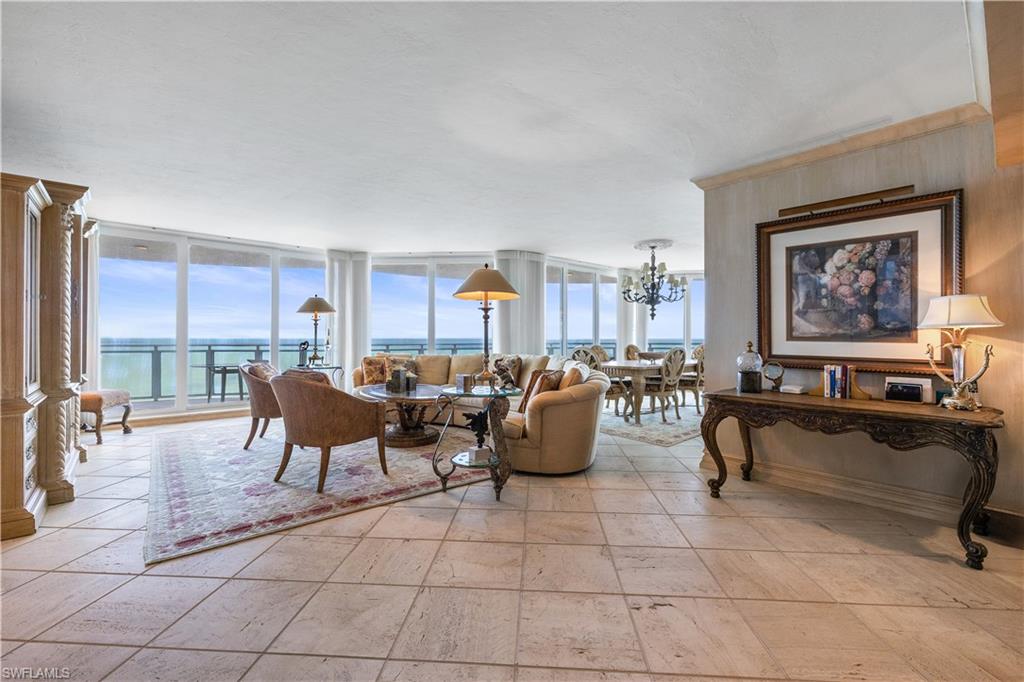 Living room with expansive windows, a water view, suspended lighting, and stone tile flooring