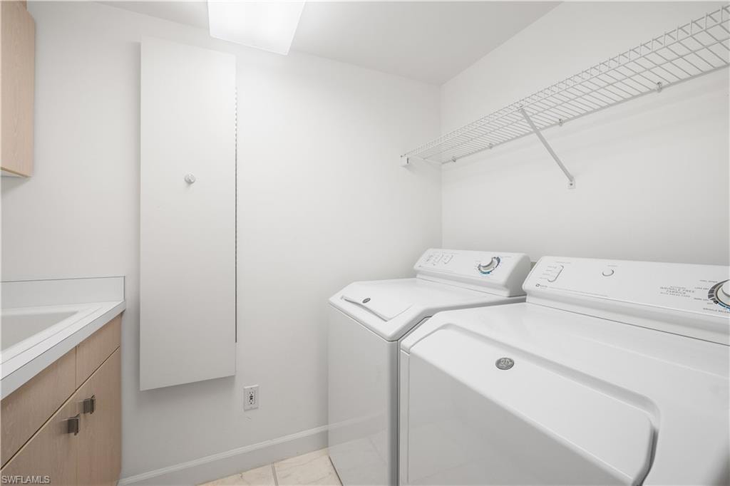 Laundry area featuring washer and dryer, cabinet space, and light marble finish flooring
