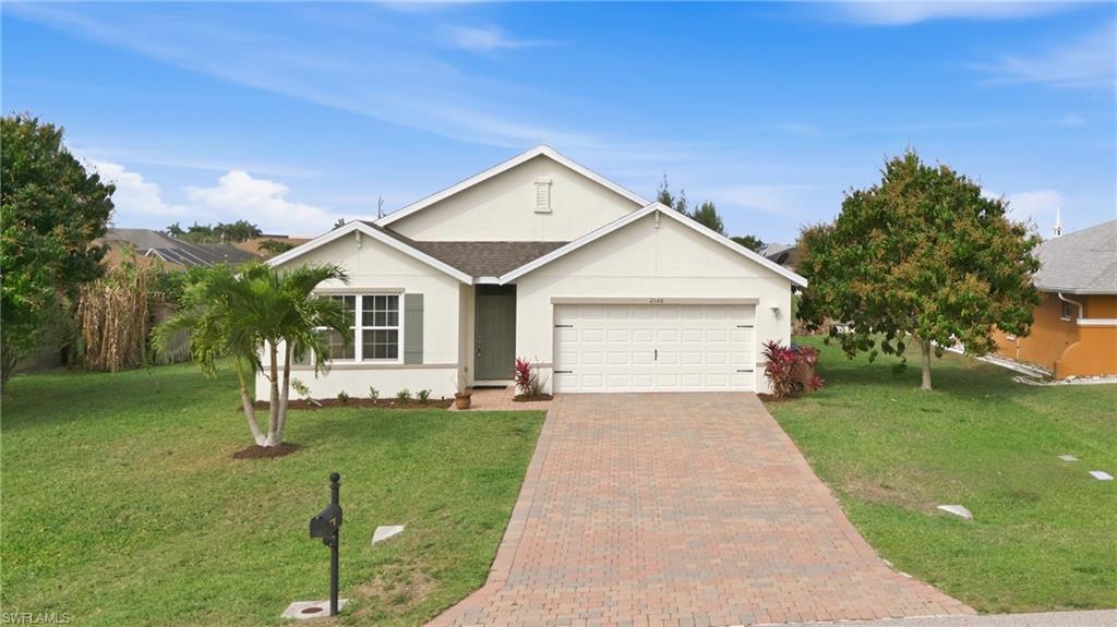 Ranch-style house featuring a front lawn, stucco siding, an attached garage, and decorative driveway