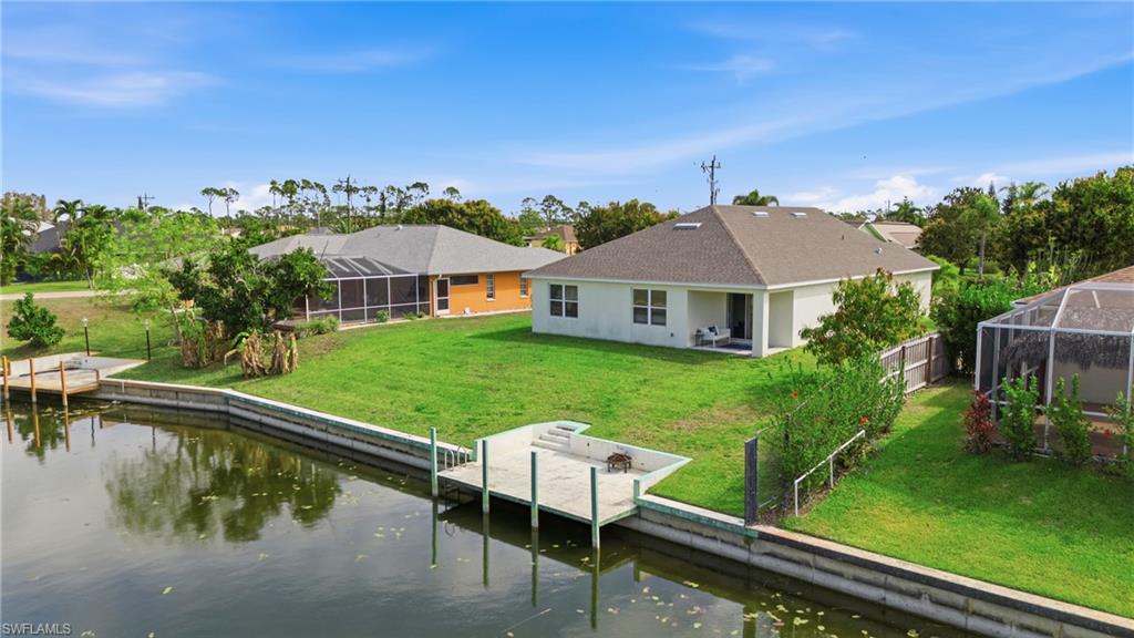 Back of house with glass enclosure, a sunroom, a water view, a lawn, and a patio area