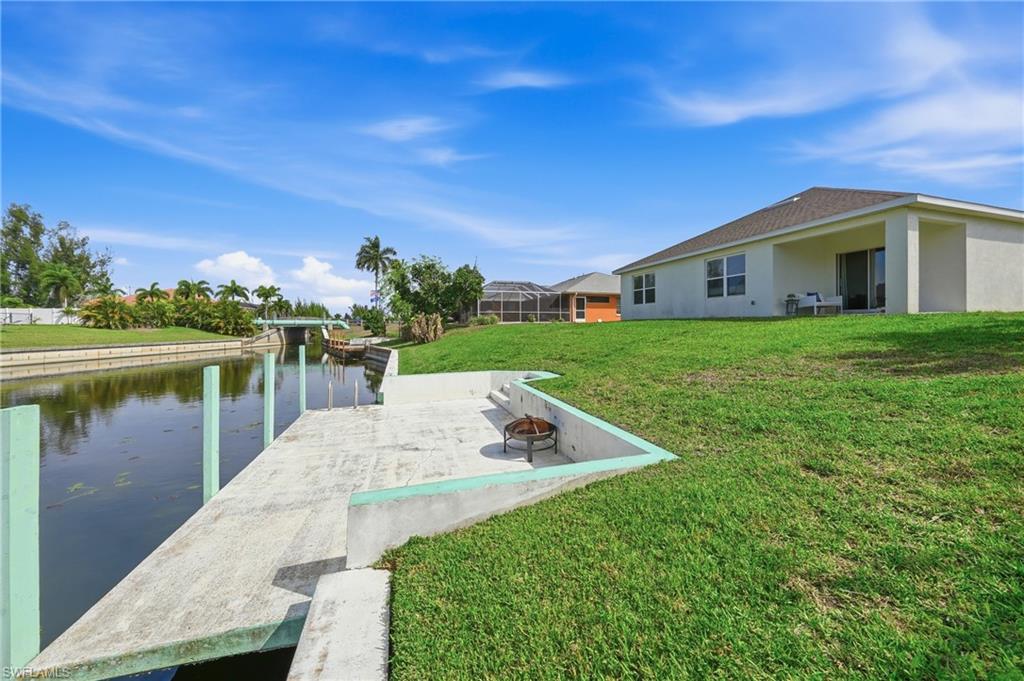 Dock area with a lawn, a water view, a fire pit, and a patio