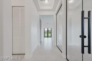 Hall featuring a tray ceiling and light tile patterned floors