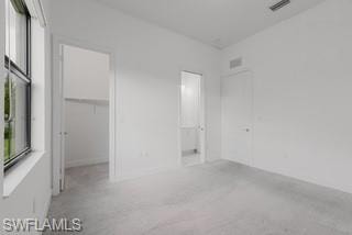 Unfurnished bedroom featuring a spacious closet, light colored carpet, and connected bathroom