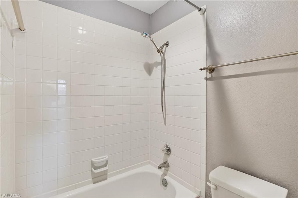 Bathroom with a textured wall and bathtub / shower combination