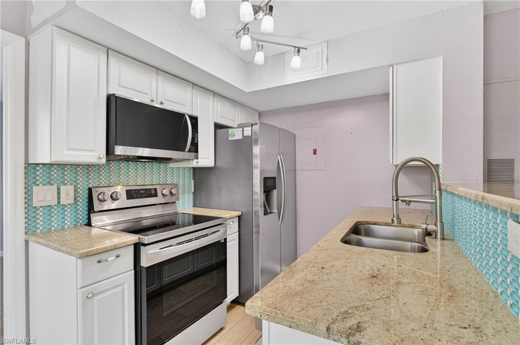 Kitchen with stainless steel appliances, white cabinets, light stone counters, and light wood-type flooring