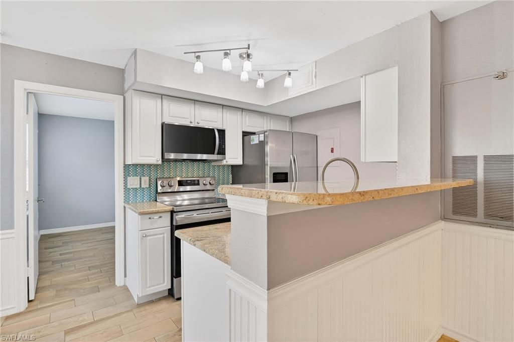 Kitchen with stainless steel appliances, white cabinets, light stone countertops, and a peninsula