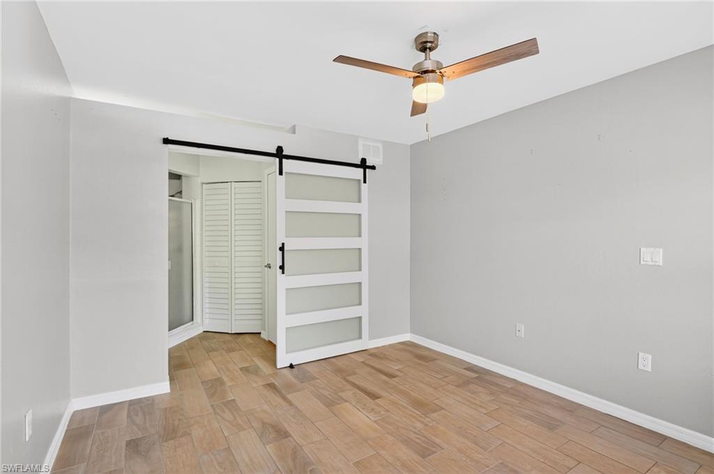 Unfurnished bedroom featuring a barn door, light wood-type flooring, a ceiling fan, and a closet