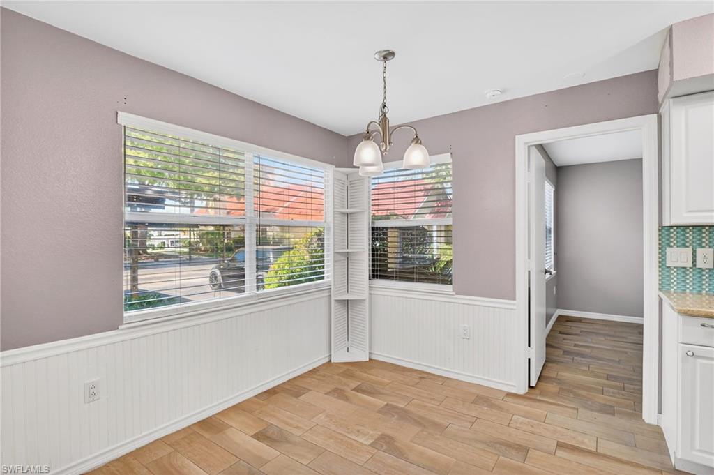 Unfurnished dining area with light wood-type flooring, a chandelier, plenty of natural light, and a wainscoted wall