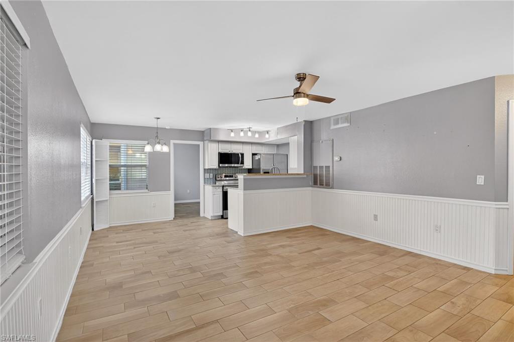 Unfurnished living room featuring a wainscoted wall, suspended lighting, a ceiling fan, and wood tiled floors