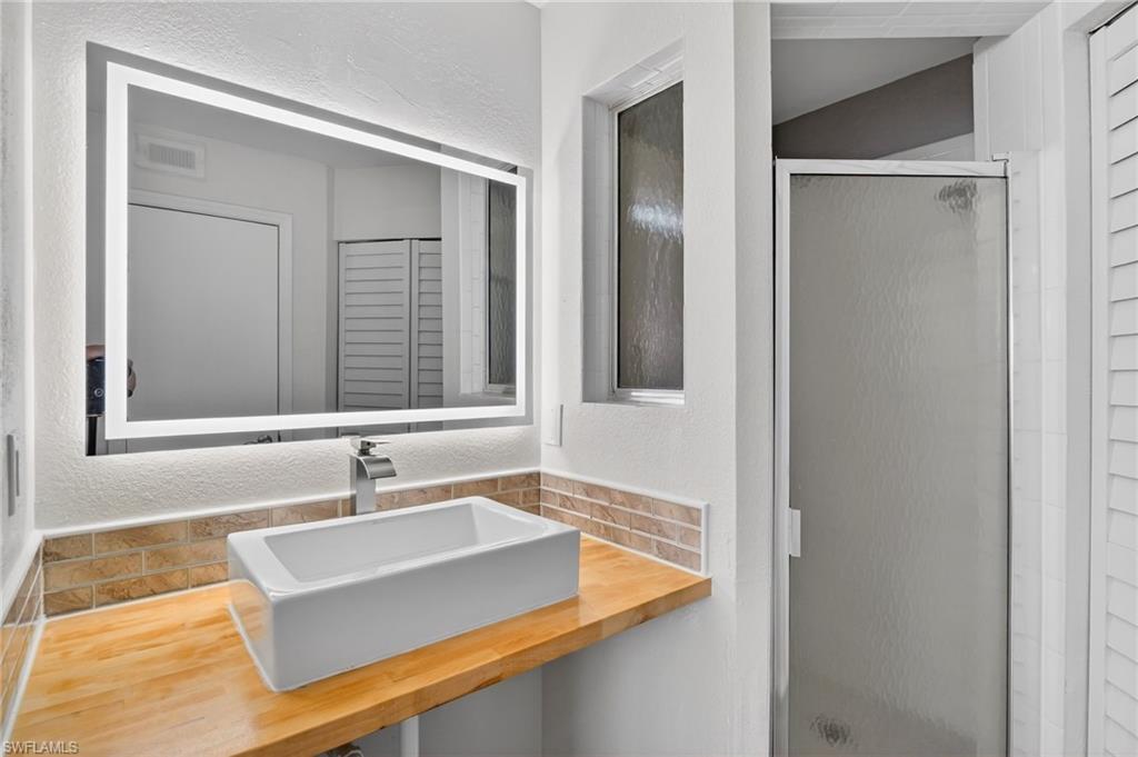 Bathroom featuring a textured wall, vanity, tasteful backsplash, a stall shower, and a closet