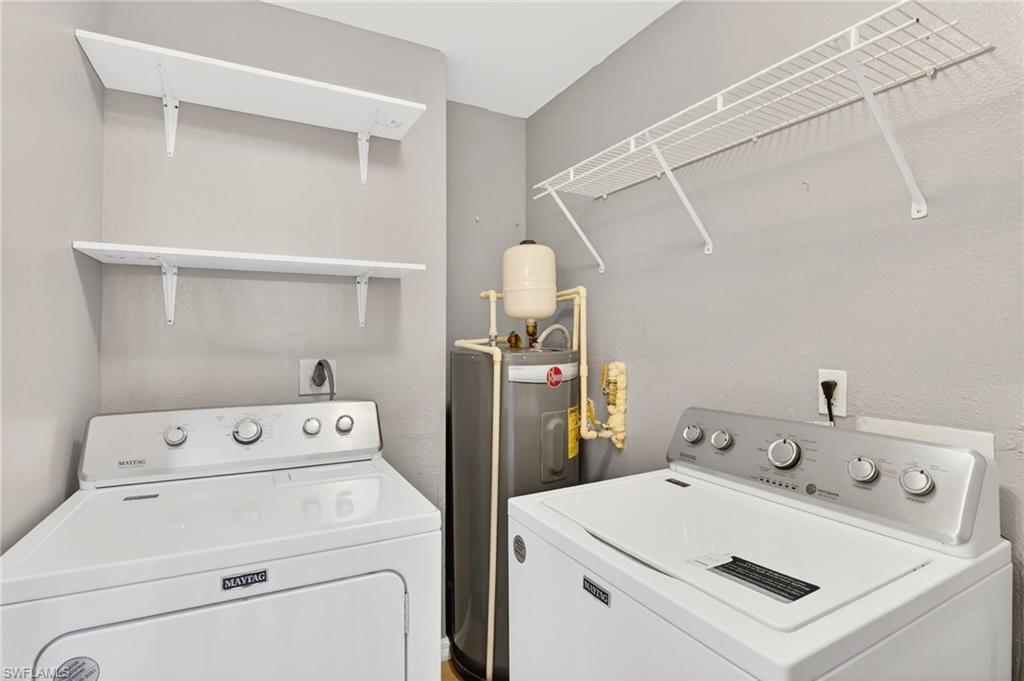 Laundry room with water heater, a textured wall, and washer and clothes dryer