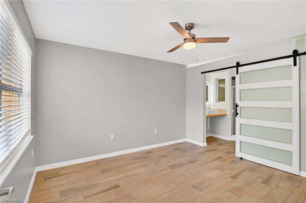 Unfurnished bedroom featuring a barn door, light wood-type flooring, a ceiling fan, and ensuite bathroom