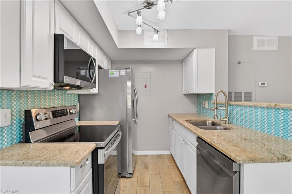 Kitchen with stainless steel appliances, light stone countertops, white cabinetry, and wood tiled floors
