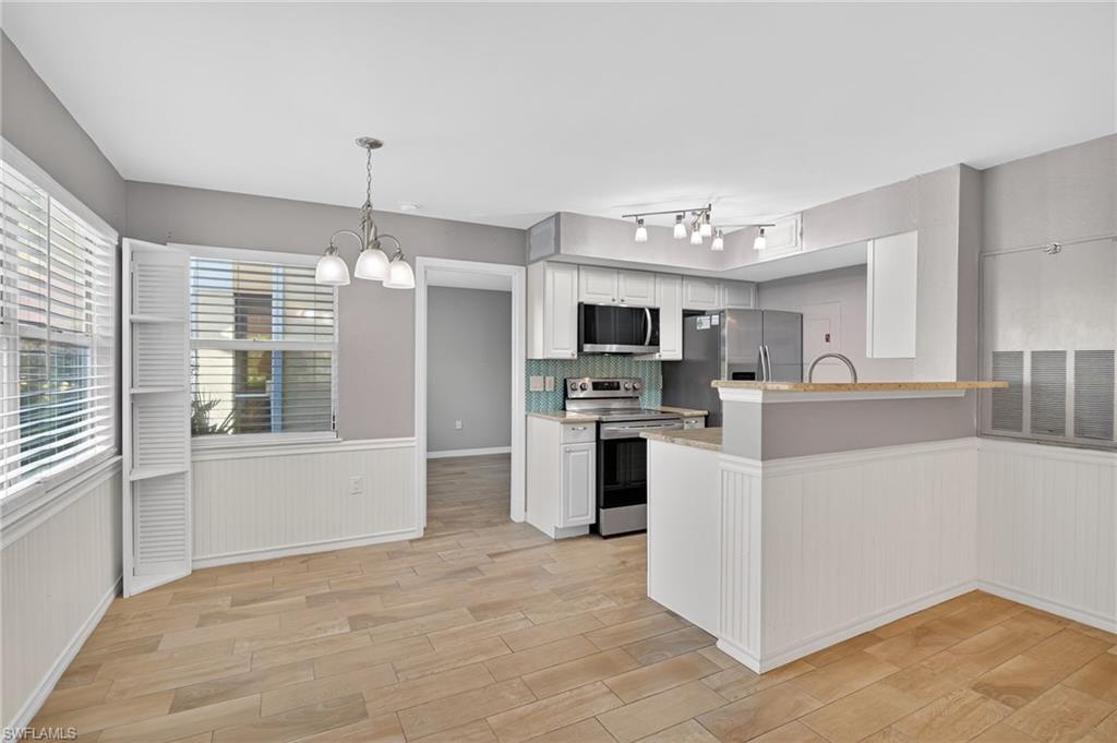 Kitchen with wainscoting, suspended lighting, stainless steel appliances, white cabinets, and light wood finished floors