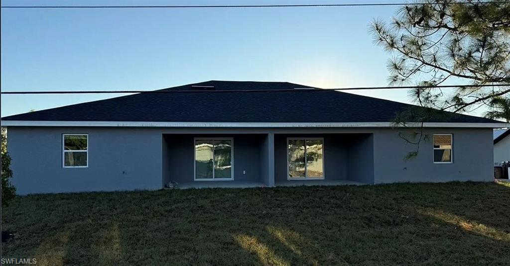 Back of house featuring stucco siding, a yard, a patio, and roof with shingles